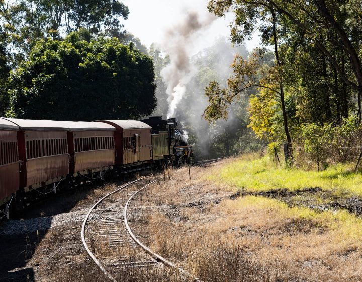 Historic Mary Valley Rattler steam engine with vintage carriages rounding a curve on the line at Maryborough, Queensland.